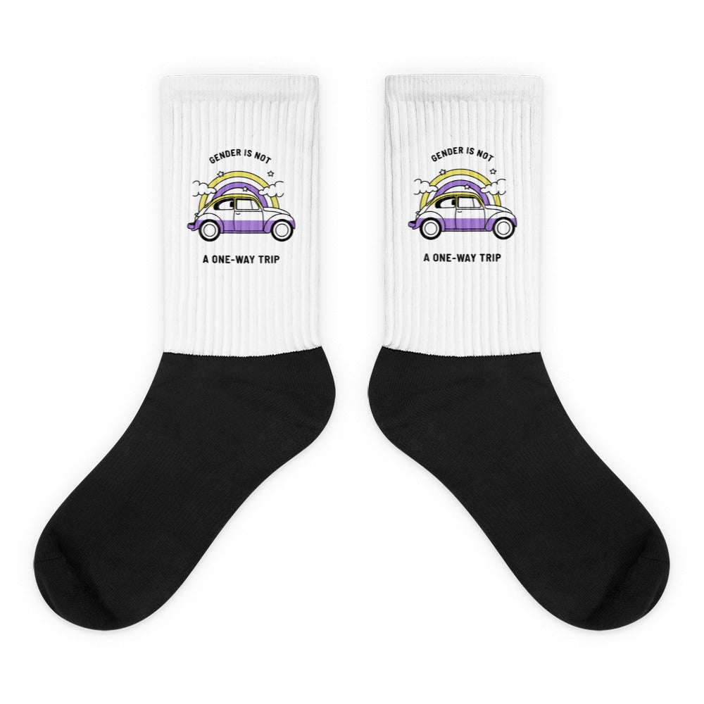Pair of black-and-white crew socks with a purple car beneath a rainbow and text reading “GENDER IS NOT A ONE-WAY TRIP”