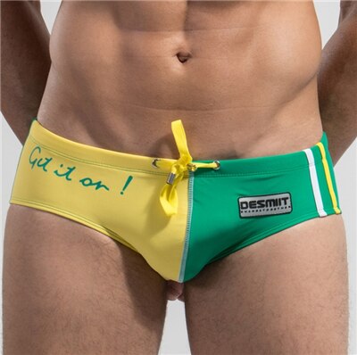 Front close-up of a person wearing yellow-and-green low-rise swim briefs with a bow