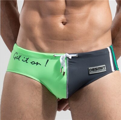 Front view of a person wearing black-and-neon-green low-rise swim briefs with “Get it on!” text
