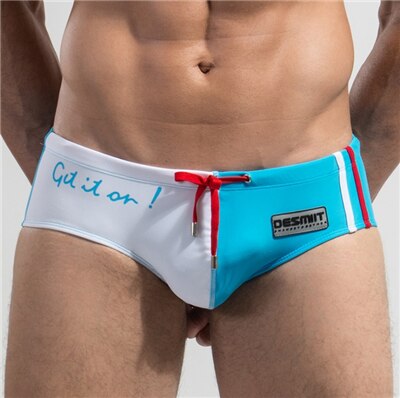 Front view of a person wearing low-rise turquoise and white swim briefs with red ties