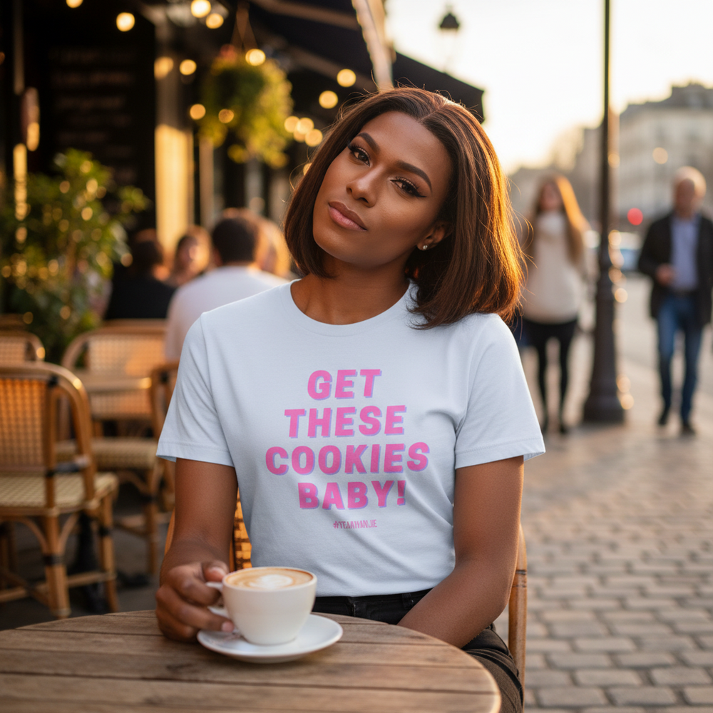 Get These Cookies Unisex T-Shirt with bold pink text is rocked by a person, chillin at a café patio with coffee