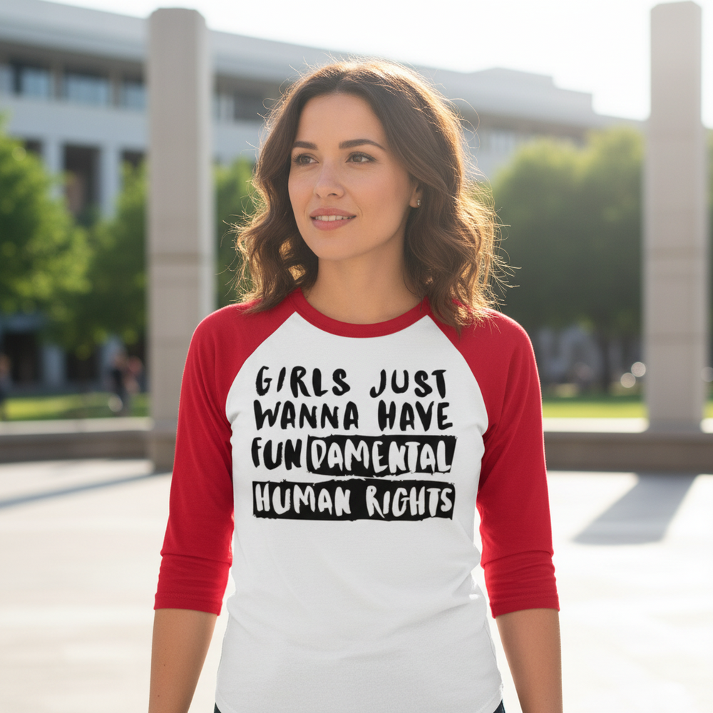 3/4 sleeve raglan shirt with "Girls Just Wanna Have Fundamental Human Rights" worn by a smiling woman in a sunny plaza.