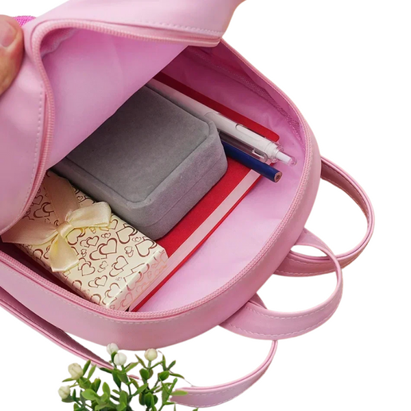 Open pink backpack showing its spacious interior, pens, notebook, case, and wrapped gift
