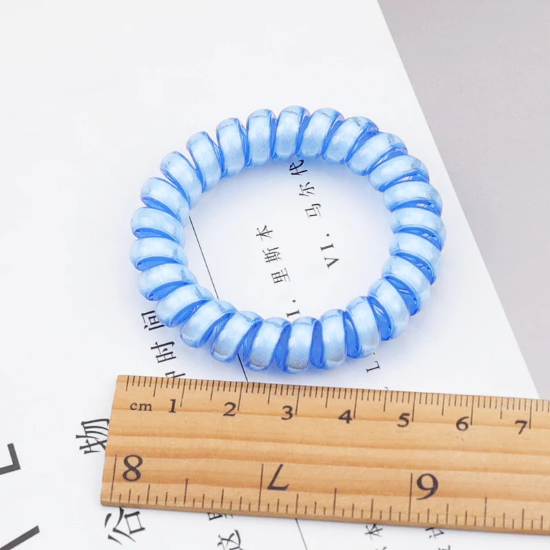 Blue translucent spiral hair tie shown flat beside a ruler for scale