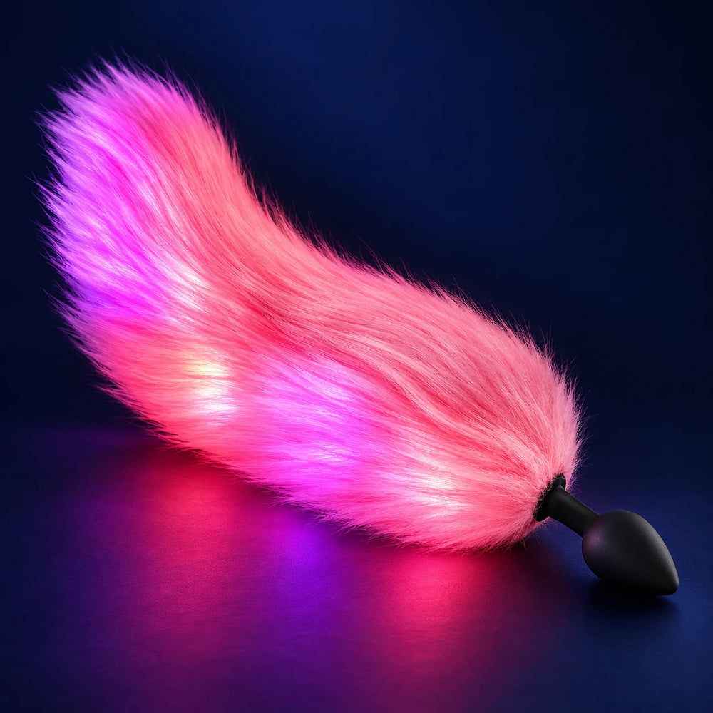 Pink GlowTails light-up furry tail butt plug illuminated pink and purple against a dark blue background.