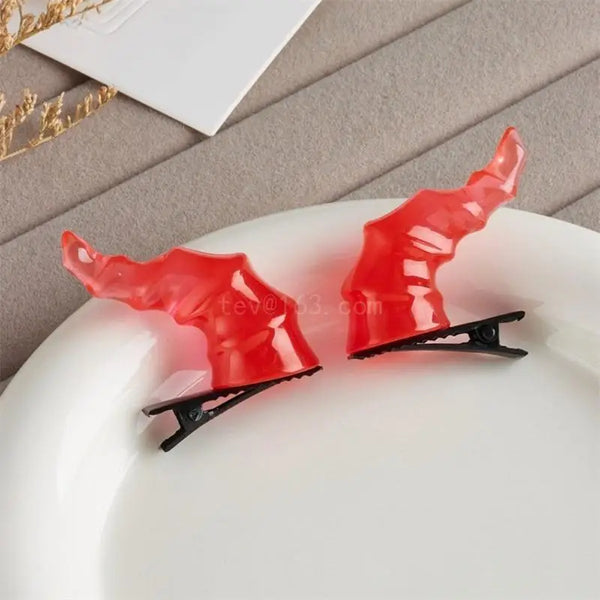 Pair of glossy red devil-horn hair clips displayed on a white plate