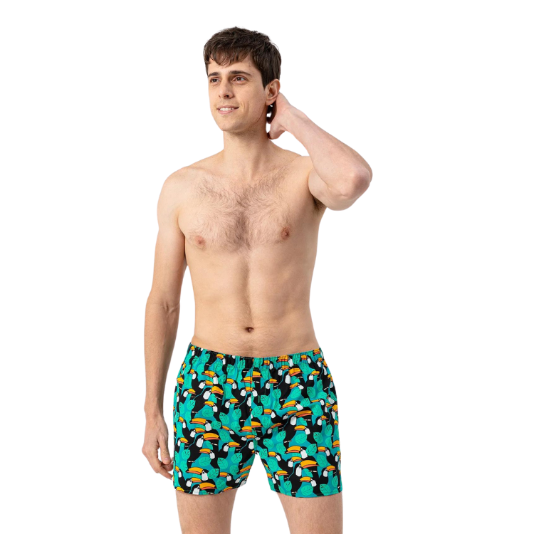 Green boxer shorts with a colorful toucan and tropical leaf print, modeled against white