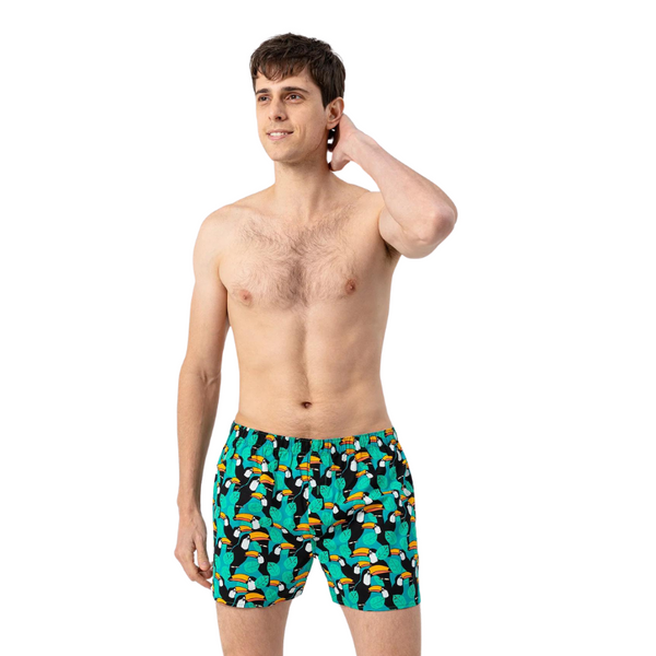 Green boxer shorts with a colorful toucan and tropical leaf print, modeled against white