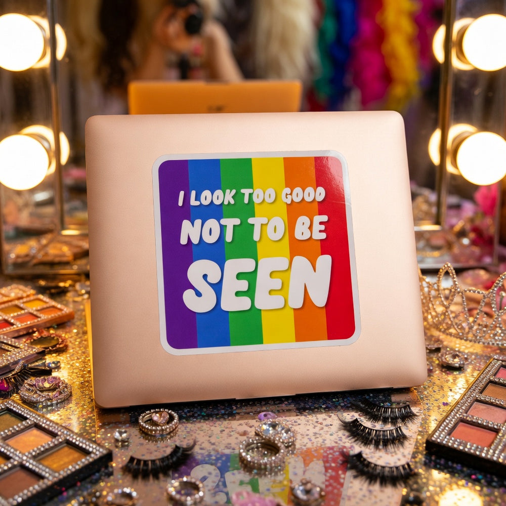 Laptop with a "I LOOK TOO GOOD NOT TO BE SEEN"—on makeup and tiara-strewn vanity; queer vibe.