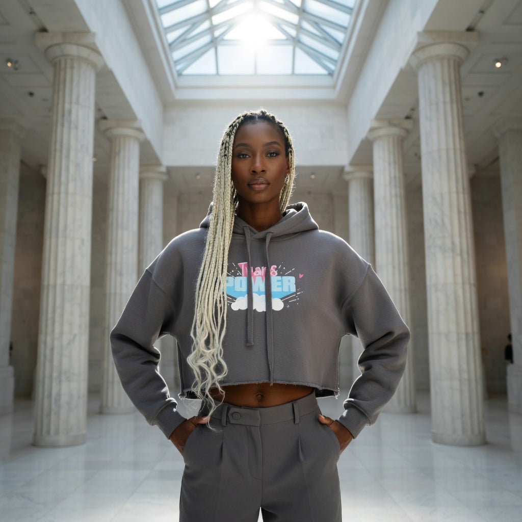 Trans Power Crop Hoodie and high-waisted pants, queer style, worn by a proud woman with blonde braids in a grand hall.