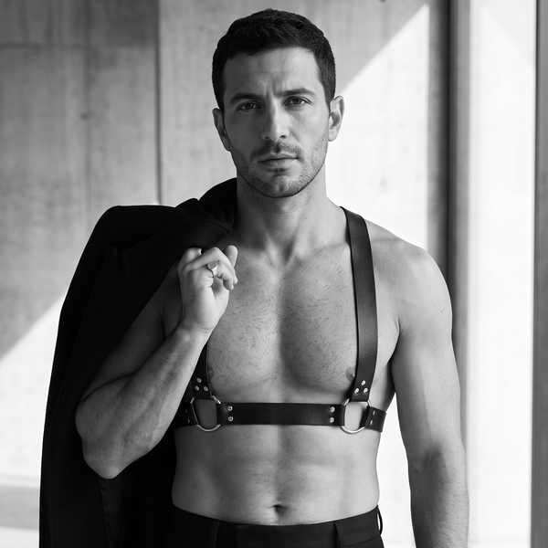 Black leather chest harness with shoulder straps and silver O-rings, worn by a model