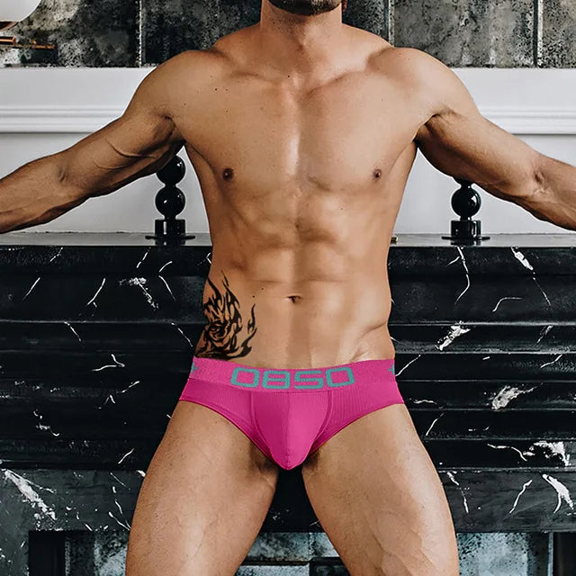 Model wearing bright pink low-rise briefs with a contrasting teal logo waistband