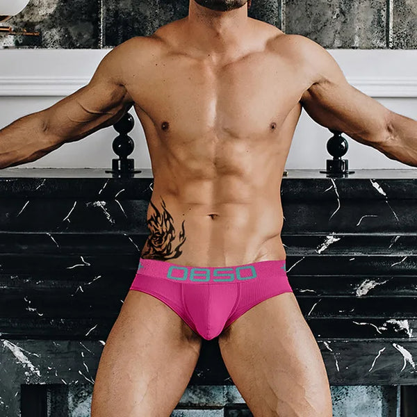 Model wearing bright pink low-rise briefs with a contrasting teal logo waistband