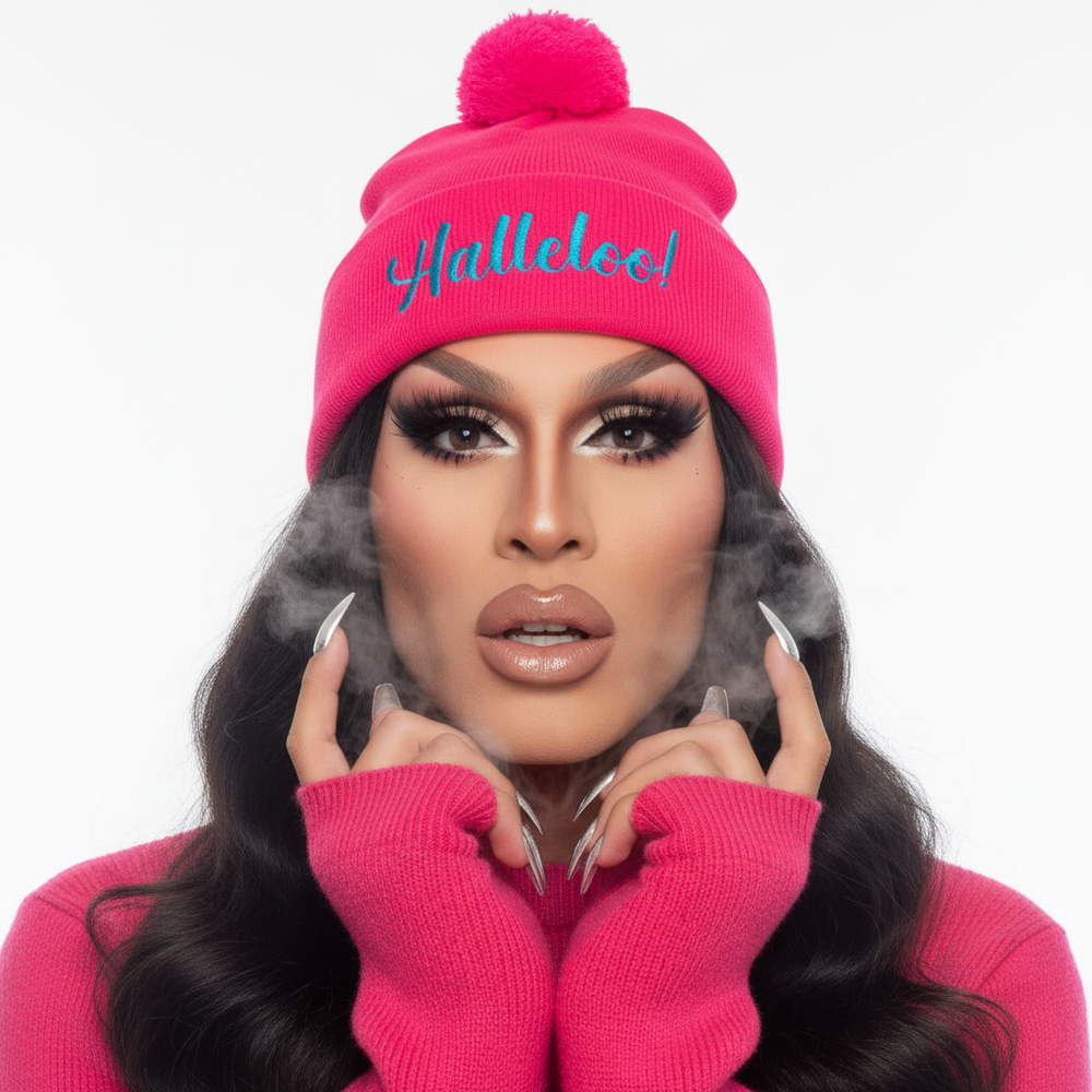 Bright pink Halleloo! Pom-Pom Beanie with blue embroidery, worn by a person in matching sweater, dramatic makeup, long nails