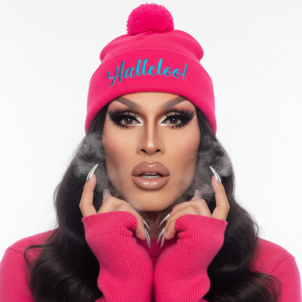 Bright pink Halleloo! Pom-Pom Beanie with blue embroidery, worn by a person in matching sweater, dramatic makeup, long nails