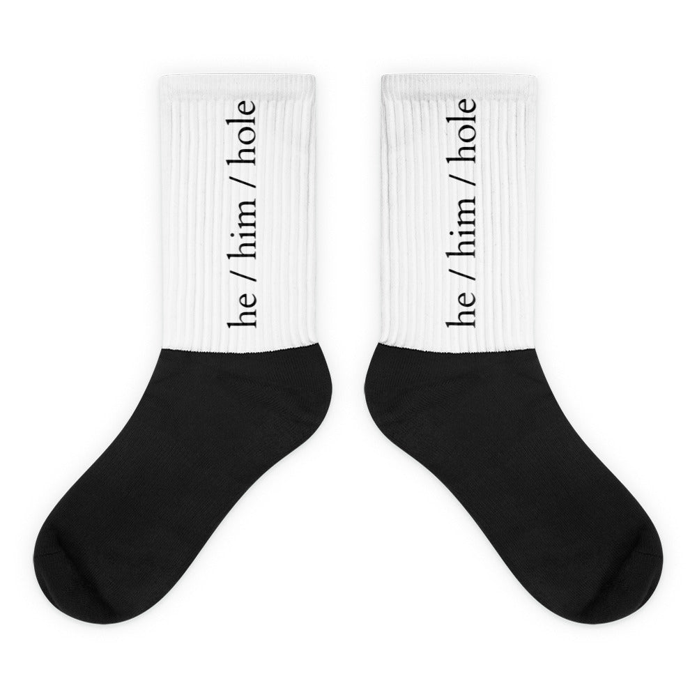 Pair of black-and-white crew socks labeled “he / him / hole” on white cuffs