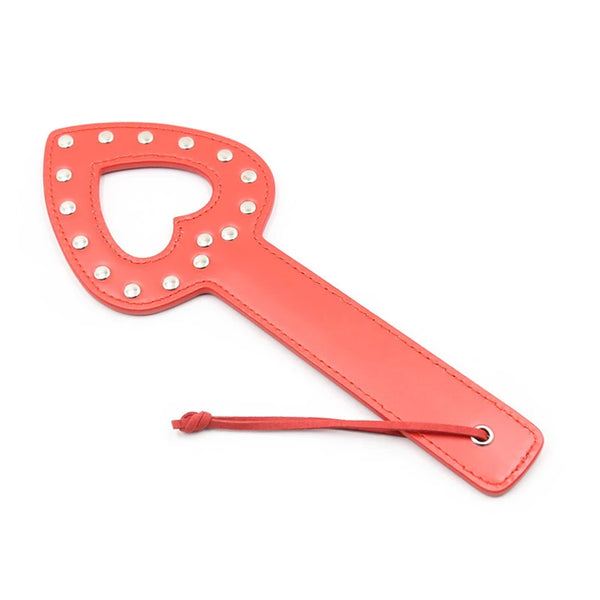 Red leather heart-cutout paddle with silver studs and a wrist strap, shown on white