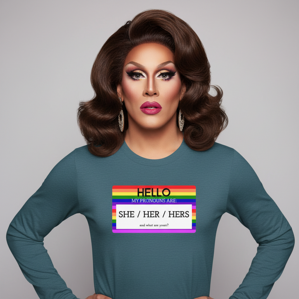 Unisex long sleeve tee reads "Hello My Pronouns Are She / Her / Hers," worn with a rainbow name tag
