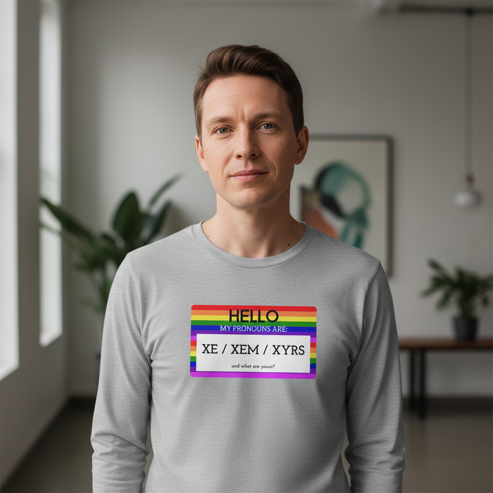 Unisex long sleeve tee reads "Hello My Pronouns Are Xe / Xem / Xyrs." Worn by someone with short brown hair indoors
