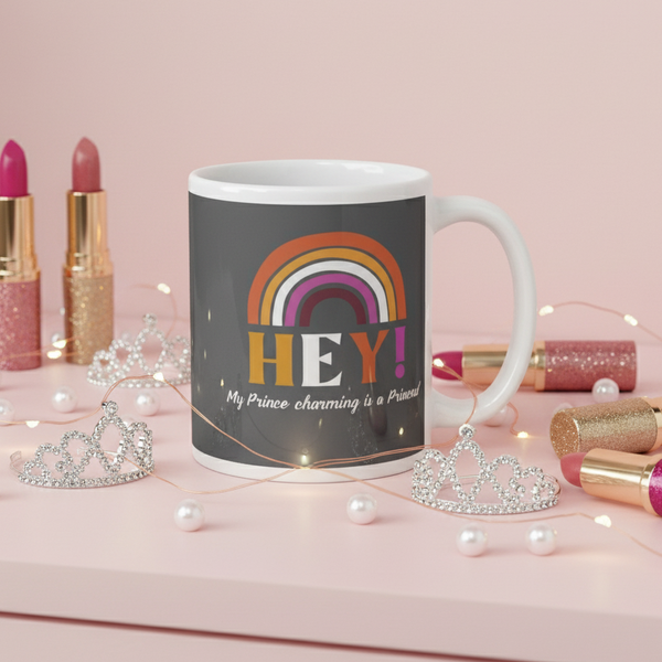 White mug reading “HEY! My Prince Charming Is a Princess!” with a rainbow, tiaras, pearls, and lipstick