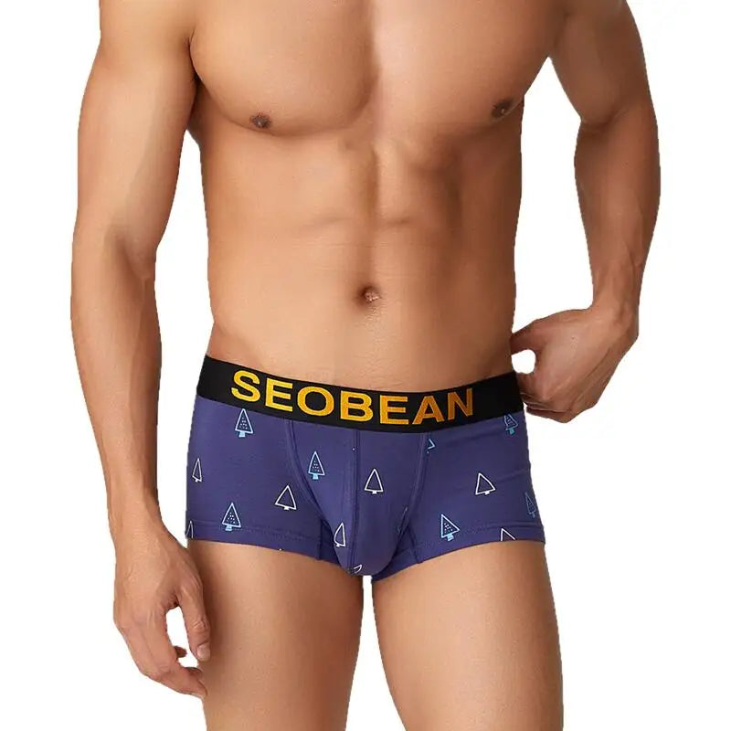 Front view of a model wearing navy Christmas tree boxer briefs with a black waistband