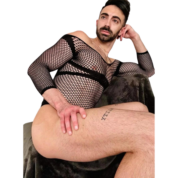 Bearded person reclining in a black fishnet long-sleeve bodysuit with exposed chest and thighs