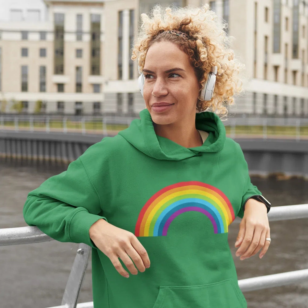 Person wearing a green hoodie with a rainbow graphic beside an urban waterfront