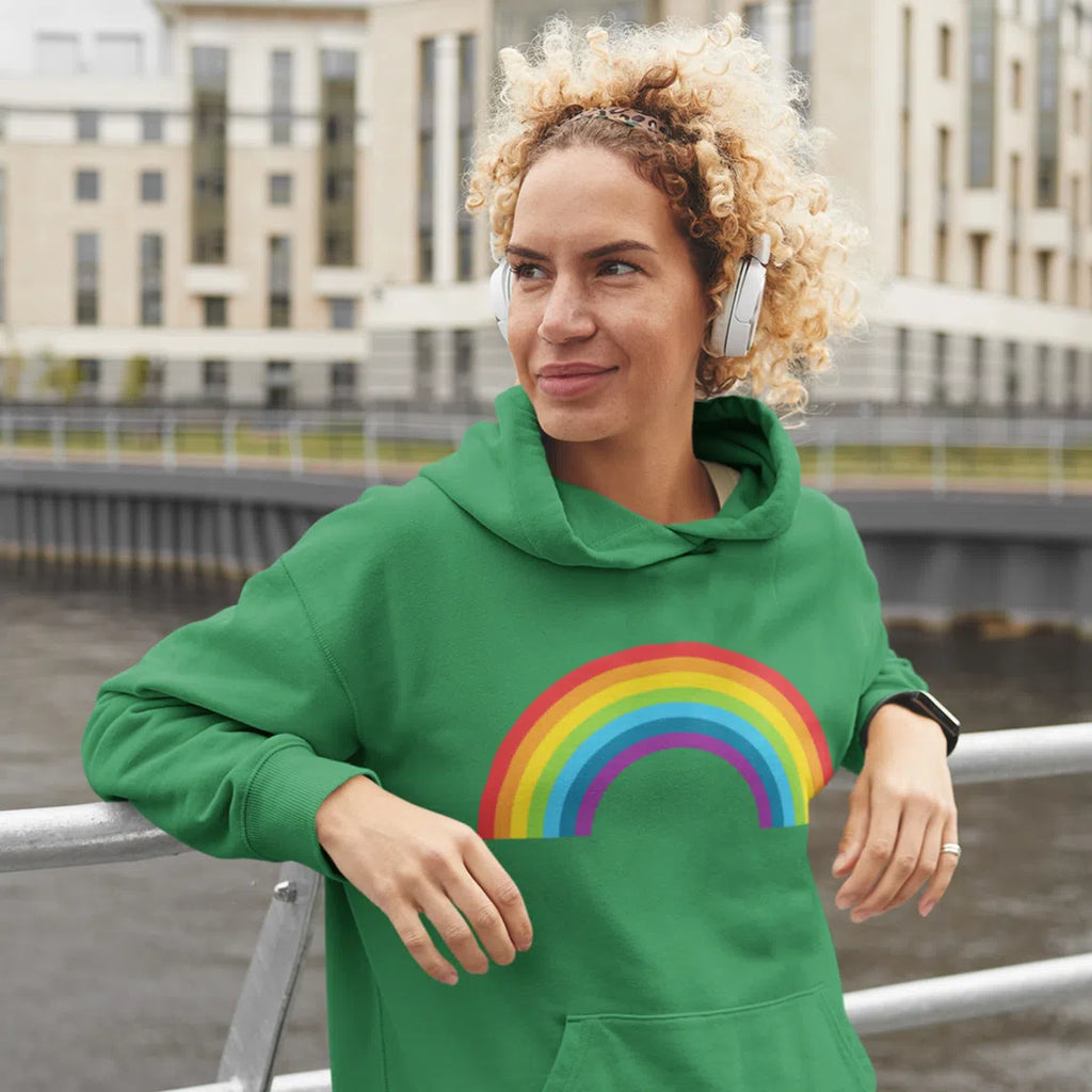 Person wearing a green hoodie with a rainbow graphic beside an urban waterfront