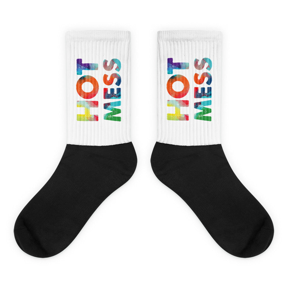 Pair of black crew socks with white cuffs and colorful vertical “HOT MESS” lettering