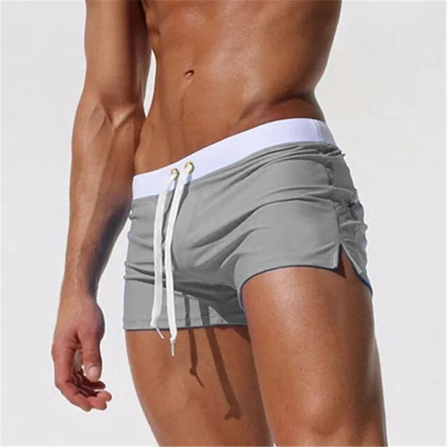 Gray low-rise men's swim shorts with a white waistband, drawstring, and side slits