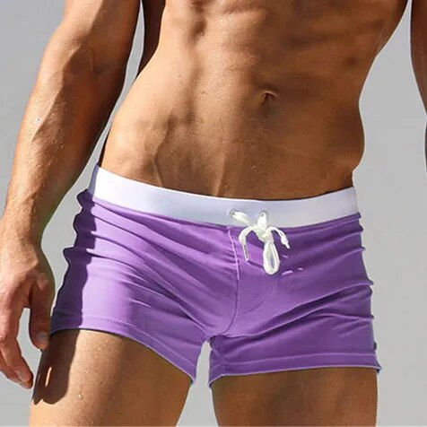 Model wearing purple low-rise swim trunks with a white waistband and drawstring