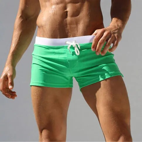 Model wearing bright green low-rise swim shorts with a white drawstring waistband