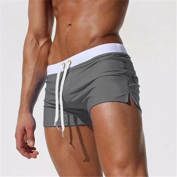 Close-up of a person wearing gray ruched swim shorts with a white drawstring waistband