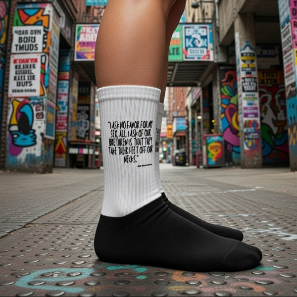 White ribbed slogan sock worn with black slip-ons on a graffiti-covered city walkway