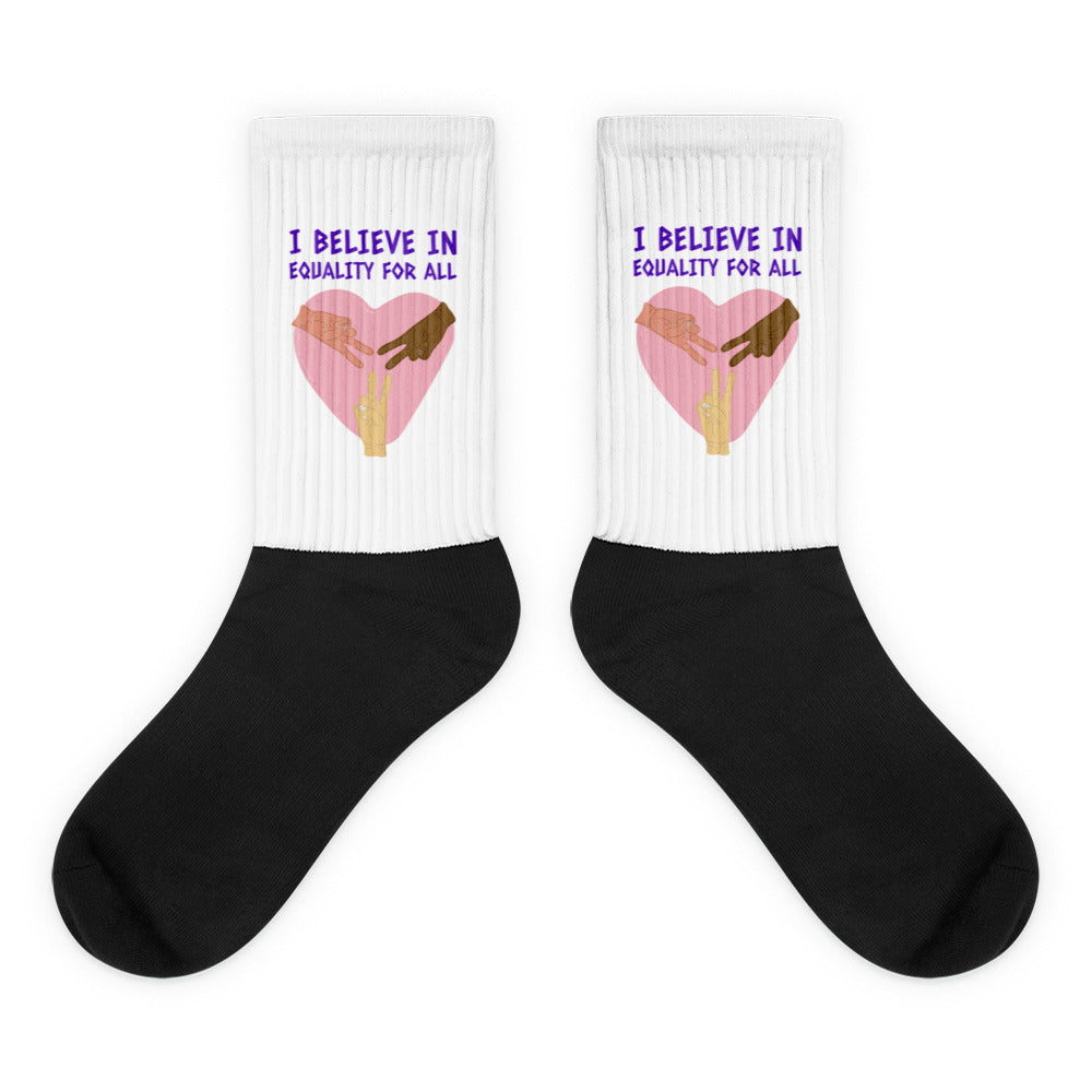Pair of crew socks with black feet and white cuffs reading “I BELIEVE IN EQUALITY FOR ALL”