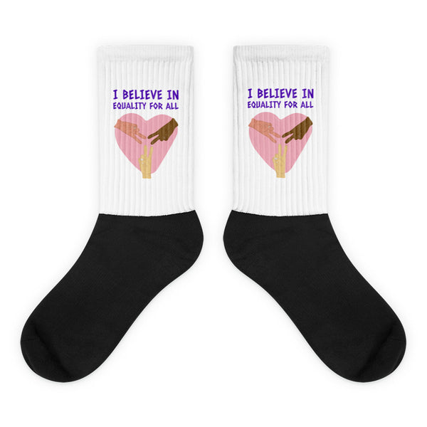 Pair of crew socks with black feet and white cuffs reading “I BELIEVE IN EQUALITY FOR ALL”