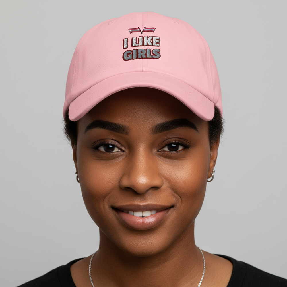 Light pink "I LIKE GIRLS" pride cap with bold, rainbow embroidery worn by a person, shown on a plain gray backdrop