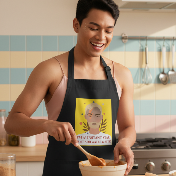 Person in a black I'm An Instant Star organic cotton apron, stirring batter with a spoon
