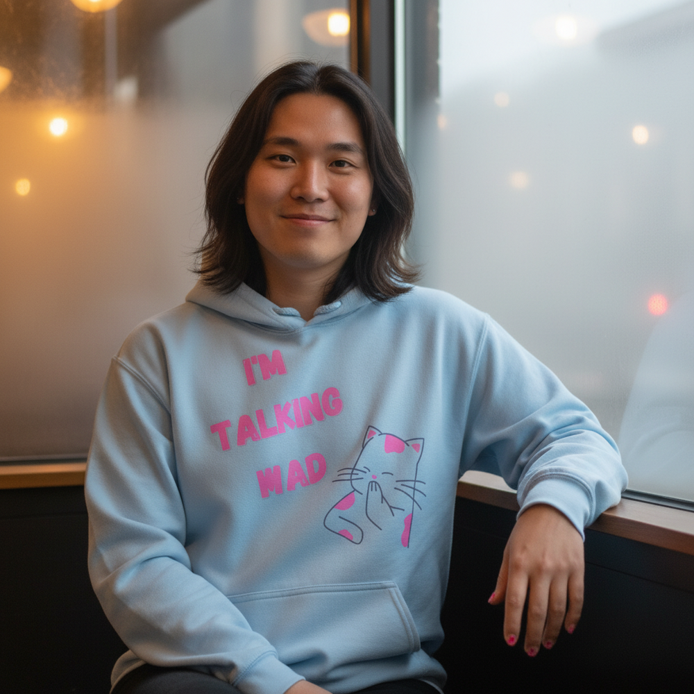 Model seated by a window wearing a light-blue hoodie reading “I'M TALKING MAD” with a cat graphic
