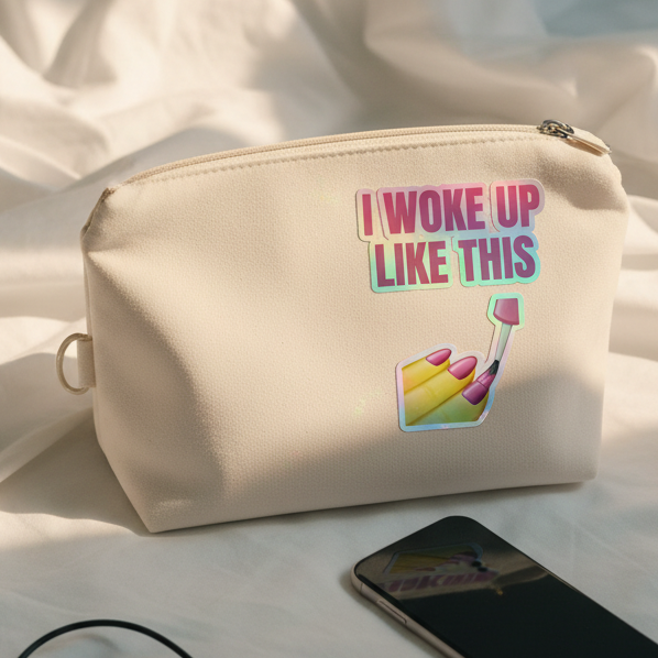Beige makeup bag on fabric, decked out with a rainbow “I Woke Up Like This” holographic sticker in pink and teal
