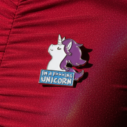 Enamel pin showing a white and purple unicorn above a blue “I’M A F***ING UNICORN” plaque