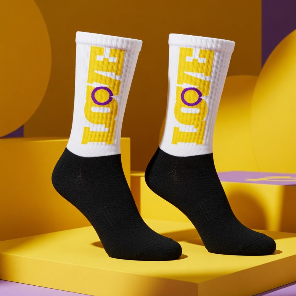 Intersex Love Socks with black feet, white uppers, "LOVE" in yellow (O as purple circle), on bold yellow and purple backdrop.