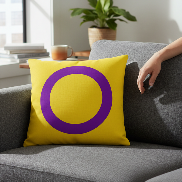 Intersex Premium Pillow with a bold purple circle on yellow sits on a gray sofa, hand nearby, potted plant, mug