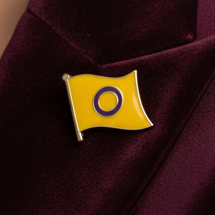 Intersex pride enamel pin with a yellow flag and purple ring emblem on dark fabric