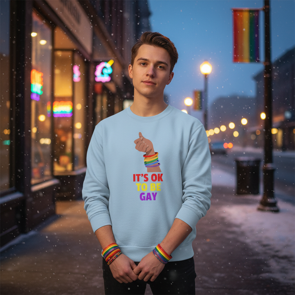 Person wearing a light blue sweatshirt reading “IT’S OK TO BE GAY,” with a rainbow-banded hand graphic