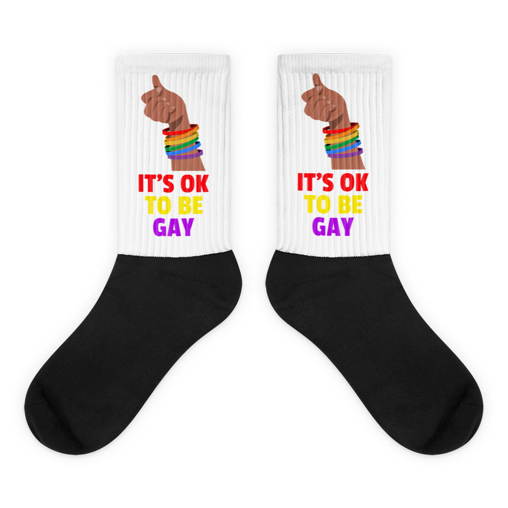 Pair of black-and-white crew socks reading “IT’S OK TO BE GAY” with rainbow wristbands