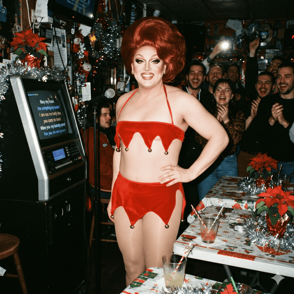 Front-facing performer models a red jingle-bell Christmas lingerie set at a festive bar