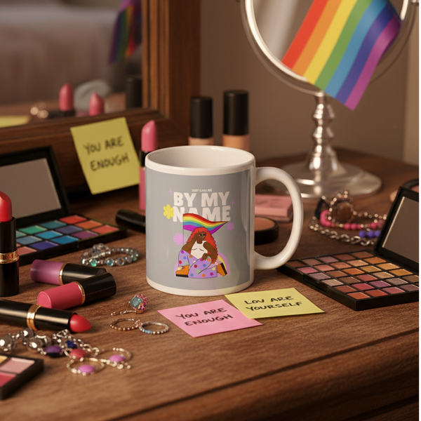 Gray mug reading “Just Call Me By My Name” beside makeup and jewelry on a vanity