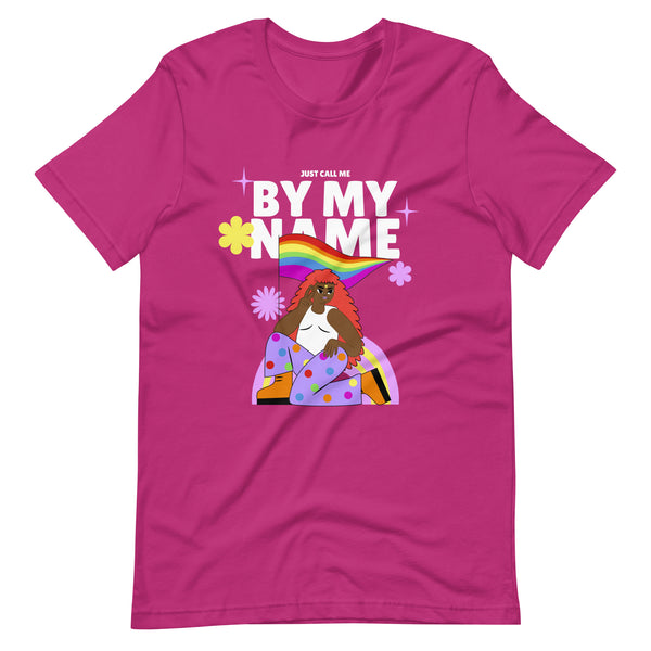 Front view of a magenta T-shirt reading “JUST CALL ME BY MY NAME,” with a rainbow flag and illustrated woman