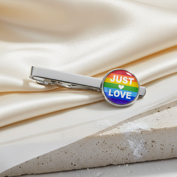 Silver tie clip with a round enamel badge of rainbow stripes and “JUST LOVE” split by a heart